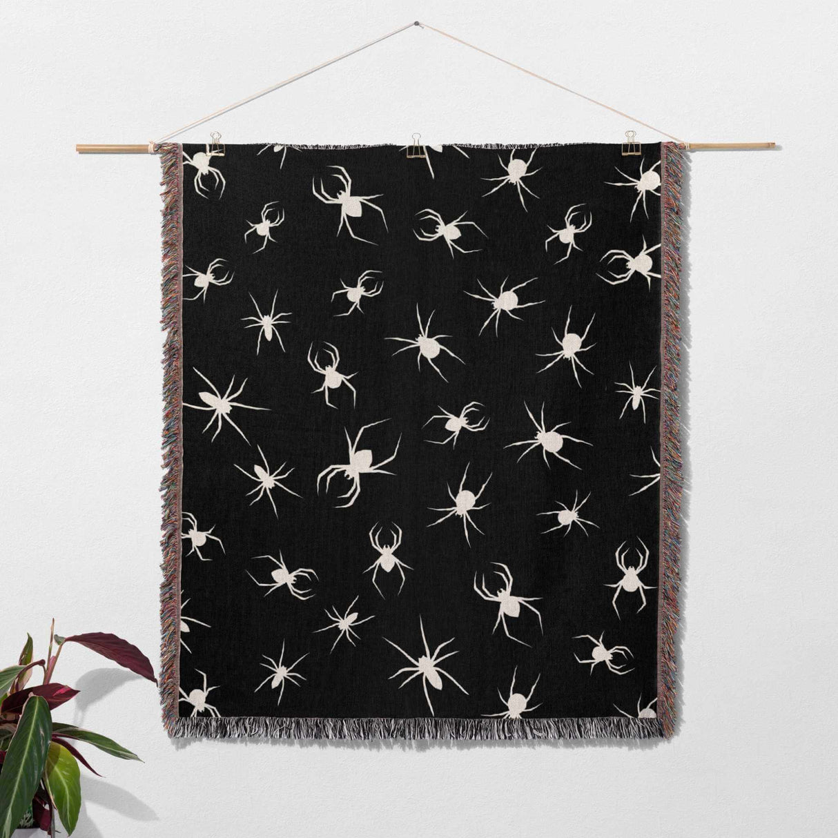 Spooky spiders halloween woven throw blanket hanging on a rod against a white wall.