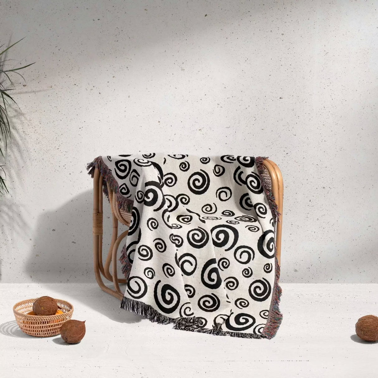 Black and white swirls patterned woven blanket throw with fringe draped over a chair on a light background.