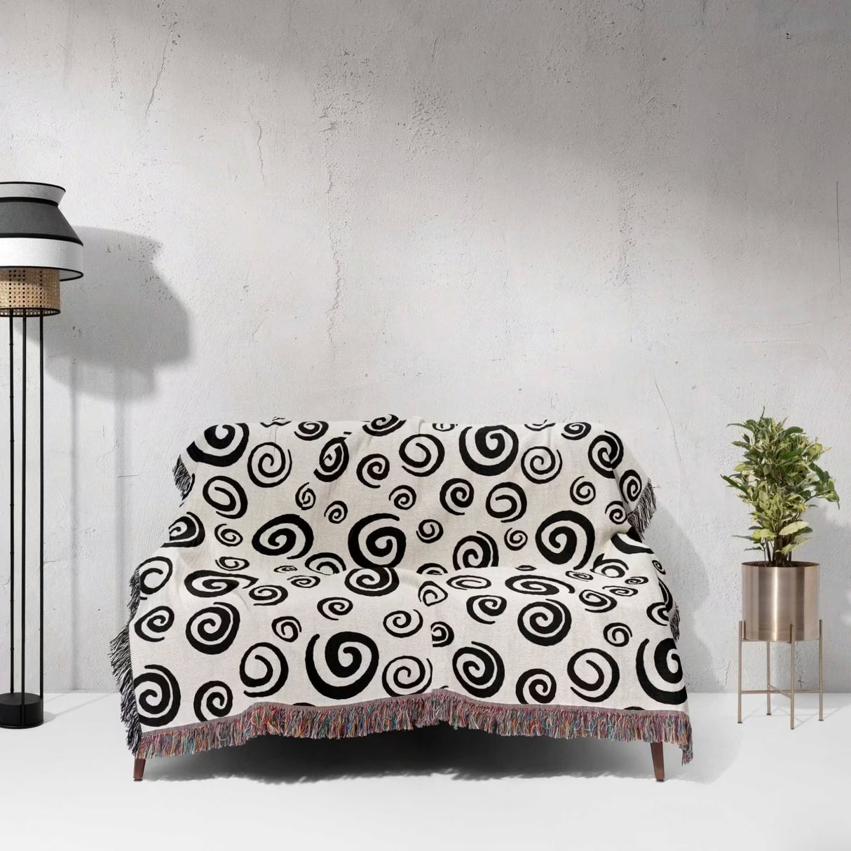 Black and white swirls patterned woven blanket throw with fringe on a couch with a white wall.