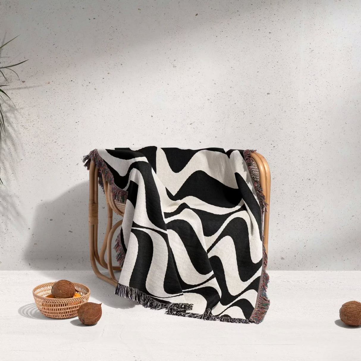 Black and white trendy abstract waves woven blanket throw tapestry draped over a wooden chair against a light gray background.
