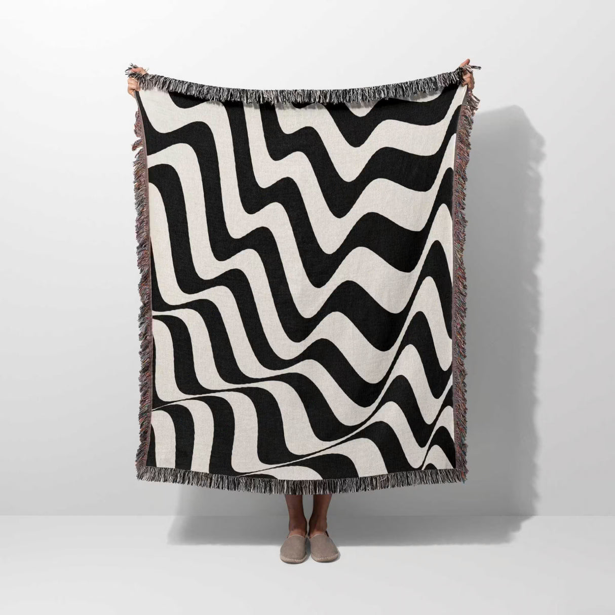 Black and white trendy abstract waves woven blanket throw tapestry held by a person on a white background.