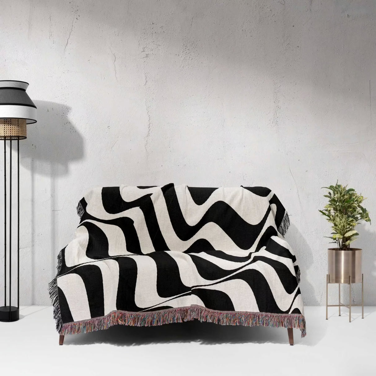 Black and white trendy abstract waves woven blanket throw tapestry on a sofa against a light gray wall.
