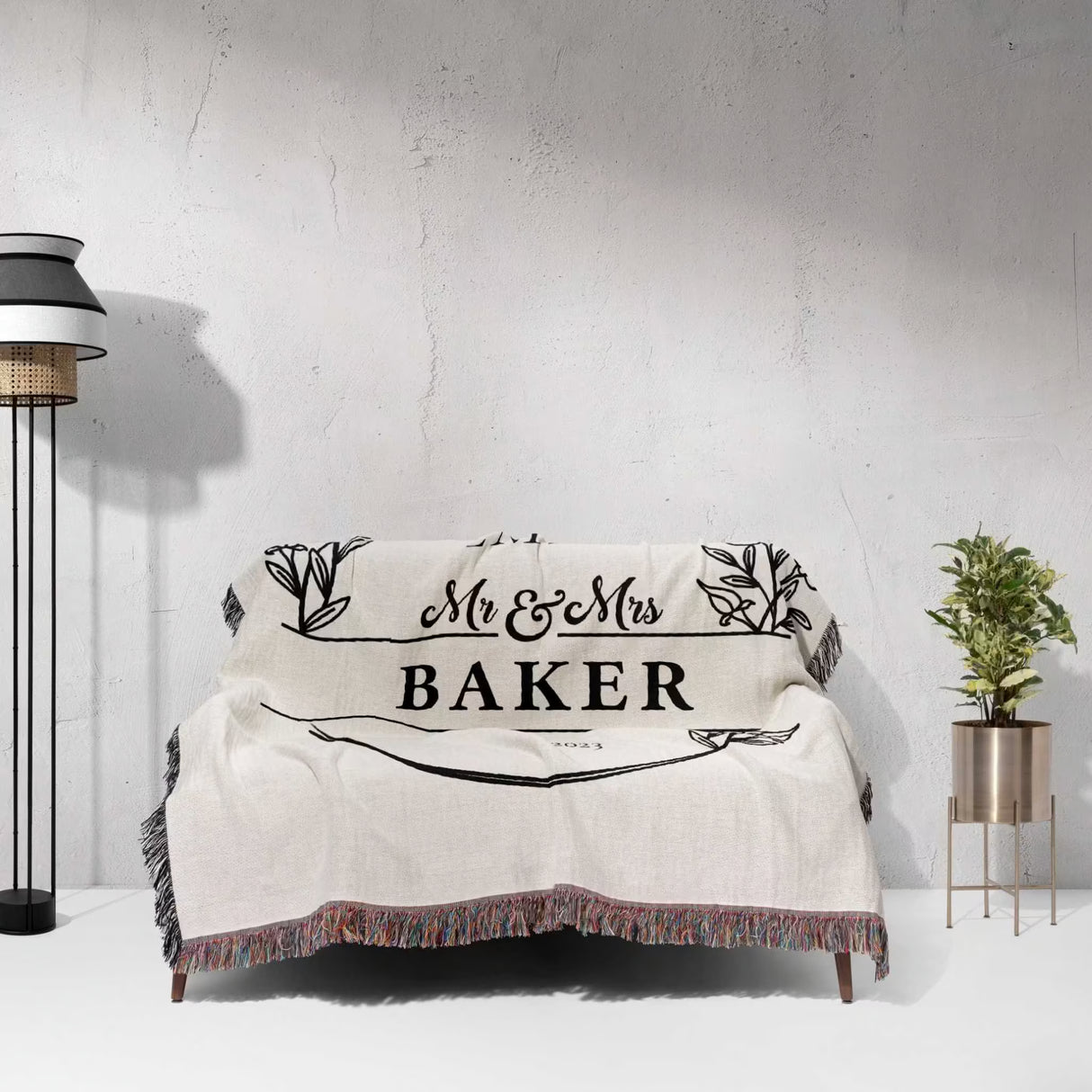 2 Year anniversary gift for wife and husband woven throw blanket  with 'Mr & Mrs Baker' text draped over a couch against a gray wall.