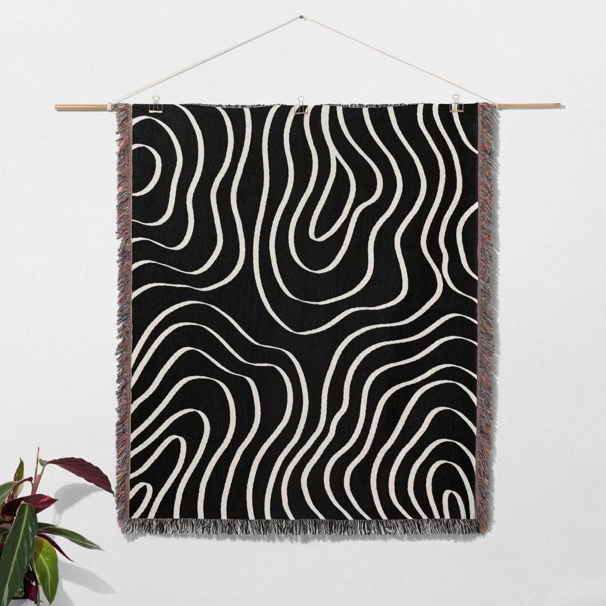Black and white abstract art waves cotton woven blanket throw tapestry hanging on a wooden rod against a white wall.