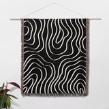 Black and white abstract art waves cotton woven blanket throw tapestry hanging on a wooden rod against a white wall.