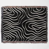 Black and white abstract art waves cotton woven blanket throw tapestry with fringed edges flat lay on a light gray background