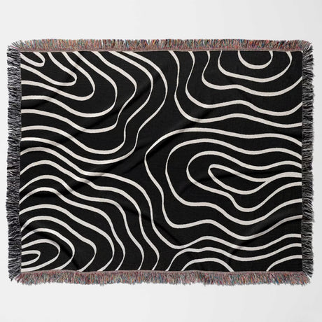 Black and white abstract art waves cotton woven blanket throw tapestry with fringed edges flat lay on a light gray background