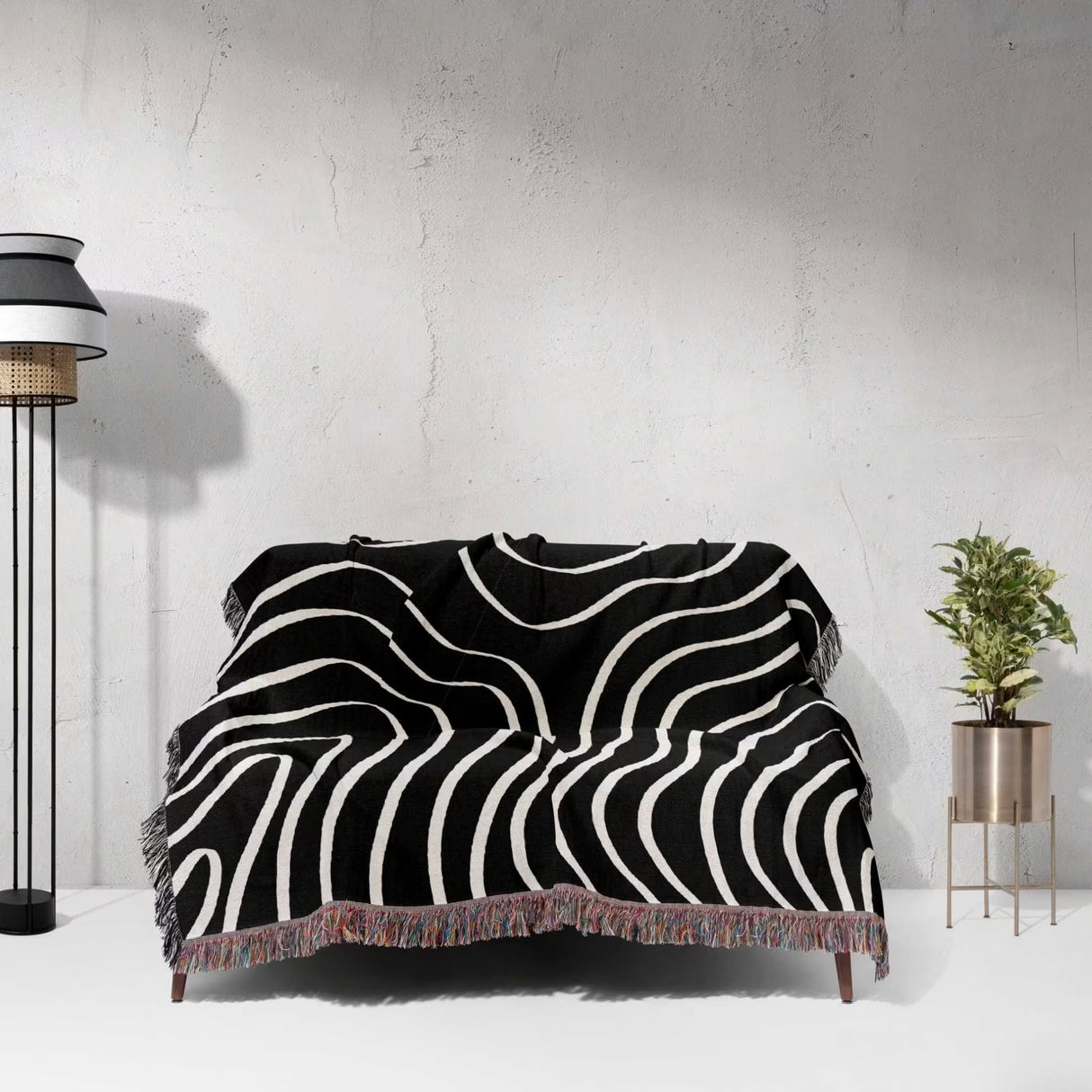Black and white abstract art waves cotton woven blanket throw tapestry draped over a couch against a gray wall.