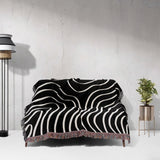 Black and white abstract art waves cotton woven blanket throw tapestry draped over a couch against a gray wall.
