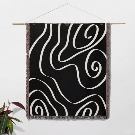 Black and white abstract art waves decorative woven blanket throw hanging on a wooden rod against a white wall.