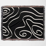 Black and white abstract art waves decorative woven blanket throw flat lay on a light gray background
