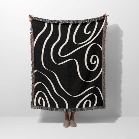 Black and white abstract art waves decorative woven blanket throw held by a person on a white background