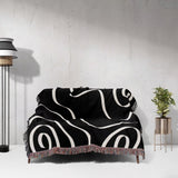 Black and white abstract art waves decorative woven blanket throw draped over a couch against a light gray wall.