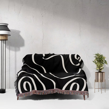 Black and white abstract art waves decorative woven blanket throw draped over a couch against a light gray wall.