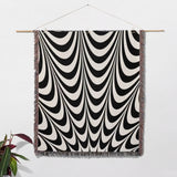 Black and white abstract art wavy woven blanket throw tapestry with multicolor fringe hanging on a wooden rod against a white wall.