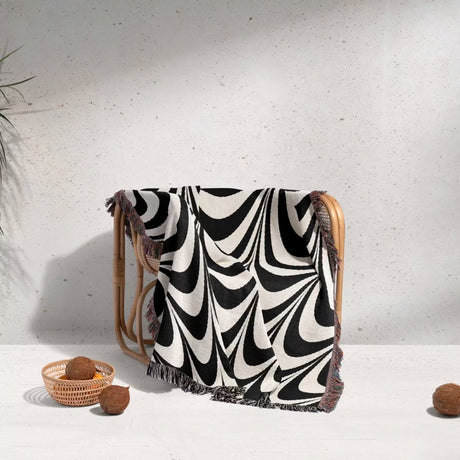 Black and white abstract art wavy woven blanket throw tapestry draped over a wooden chair against a light gray wall.