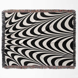 Black and white abstract art wavy woven blanket throw tapestry with fringed edges flat lay on a white background.