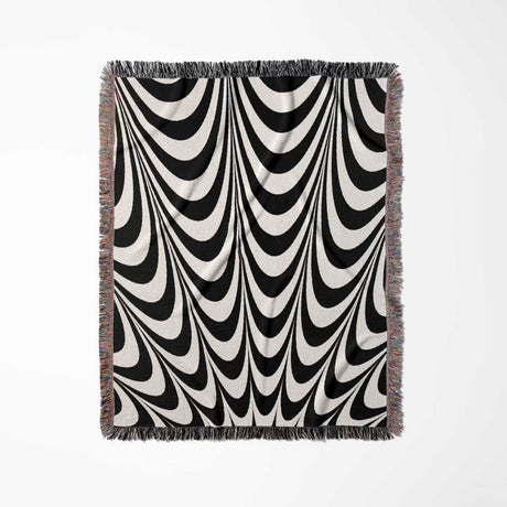 Black and white abstract art wavy woven blanket throw tapestry with fringe full view on a light gray background.