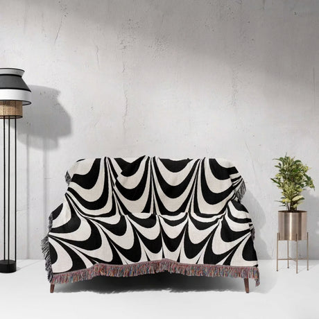 Black and white abstract art wavy woven blanket throw tapestry draped over a couch against a light gray wall.