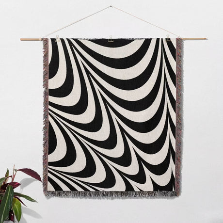 Black and white abstract modern artistic woven blanket throw tapestry hanging on a wooden rod against a white wall.