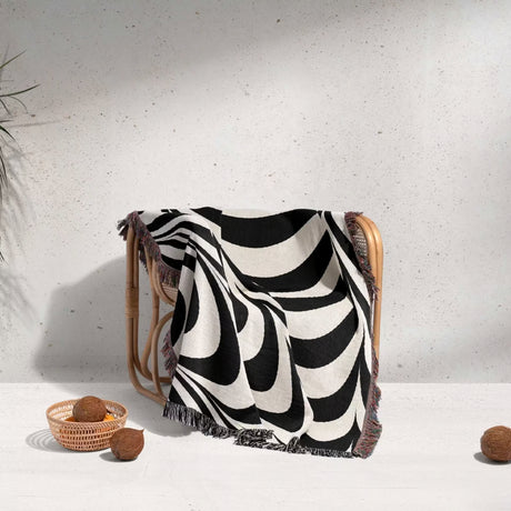 Black and white abstract modern artistic woven blanket throw tapestry draped over a chair against a light gray wall.