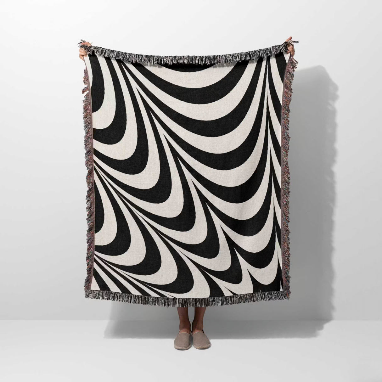 Black and white abstract modern artistic woven blanket throw tapestry held by a person on a white background.