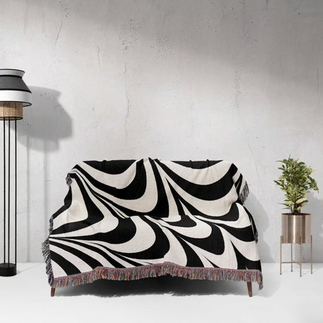 Black and white abstract modern artistic woven blanket throw tapestry draped over a couch against a light gray wall.