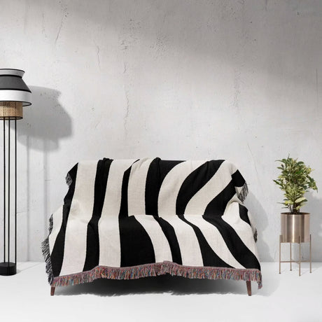 Black and white abstract shapes woven blanket throw tapestry draped over a couch against a light gray wall.