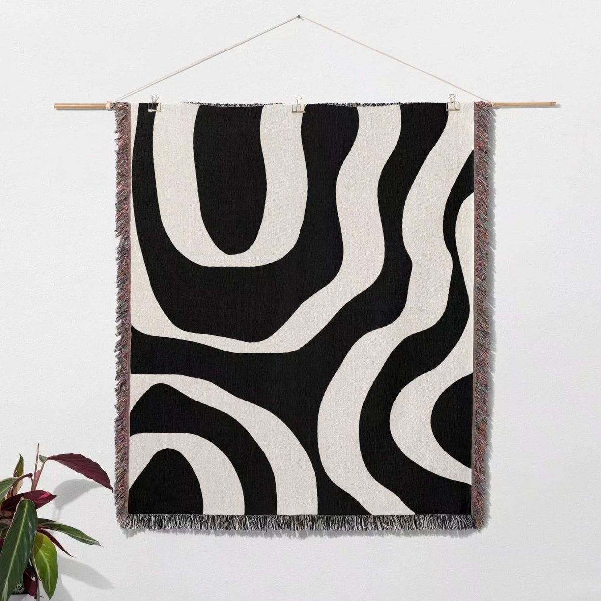 Black and white abstract waves aesthetic woven blanket throw hanging on a wooden rod against a white wall.