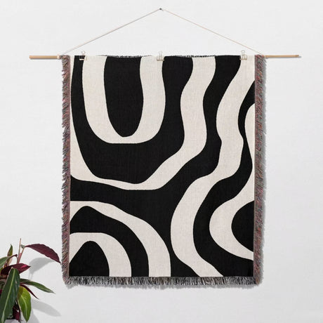 Black and white abstract waves aesthetic woven blanket throw hanging on a wooden rod against a white wall.