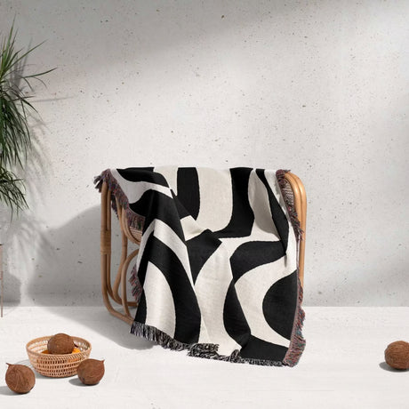 Black and white abstract waves aesthetic woven blanket throw draped over a chair with a minimal background.