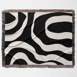 Black and white abstract waves aesthetic woven blanket throw with fringed edges flat lay on a white background.