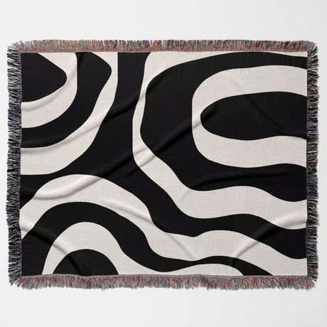 Black and white abstract waves aesthetic woven blanket throw with fringed edges flat lay on a white background.