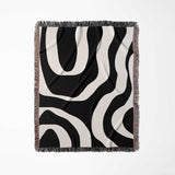 Black and white abstract waves aesthetic woven blanket throw with fringe full view on a light gray background.