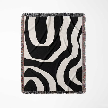 Black and white abstract waves aesthetic woven blanket throw with fringe full view on a light gray background.