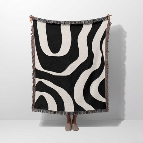 Person holding a black and white abstract waves aesthetic woven blanket throw against a white background.