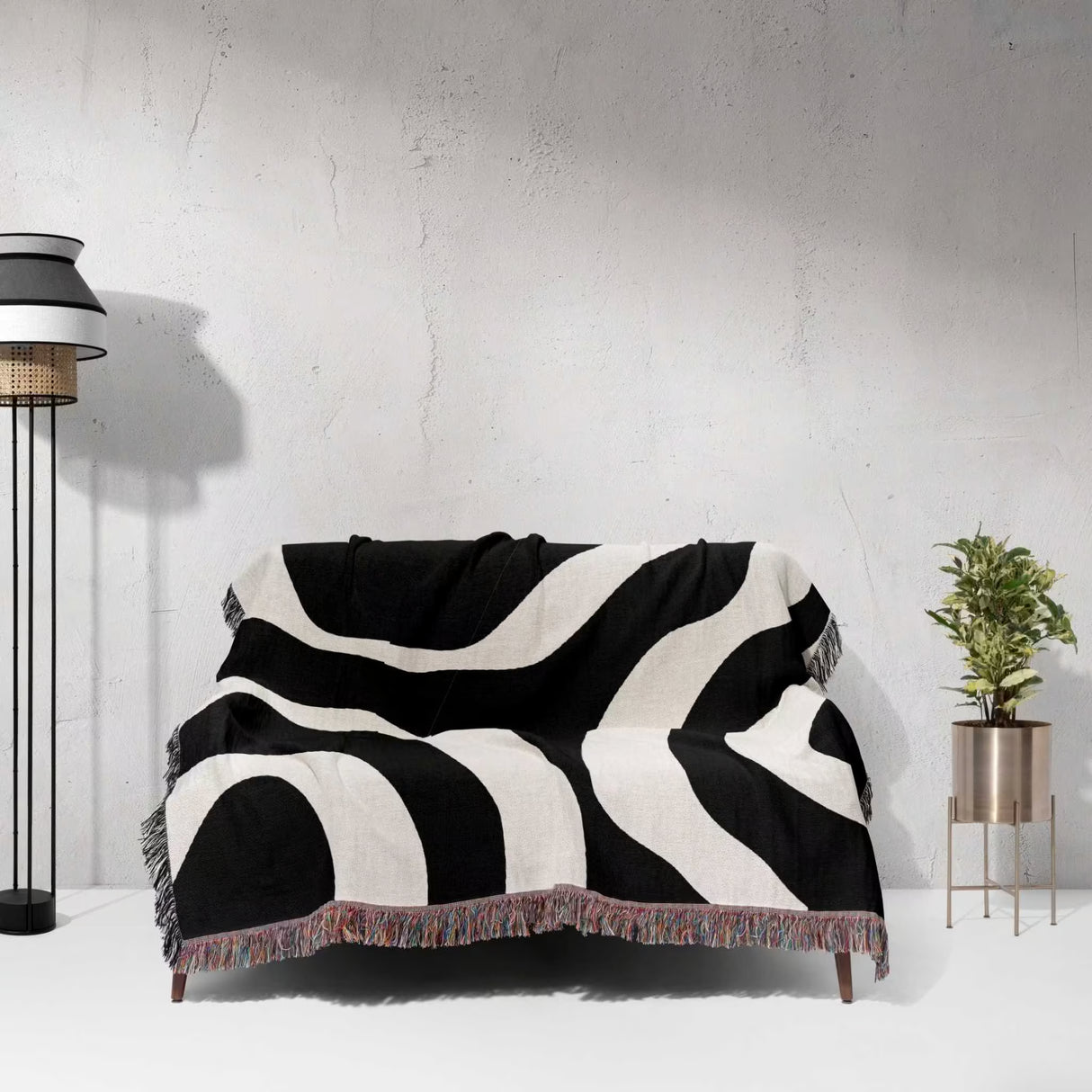 Black and white abstract waves aesthetic woven blanket throw on a sofa against a light gray wall.