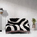 Black and white abstract waves aesthetic woven blanket throw on a sofa against a light gray wall.