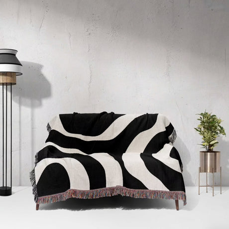 Black and white abstract waves aesthetic woven blanket throw on a sofa against a light gray wall.