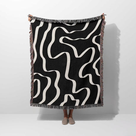 Person holding a black and white abstract waves artistic woven blanket throw against a white background