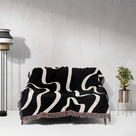 Black and white abstract waves artistic woven blanket throw draped over a sofa against a light gray wall.