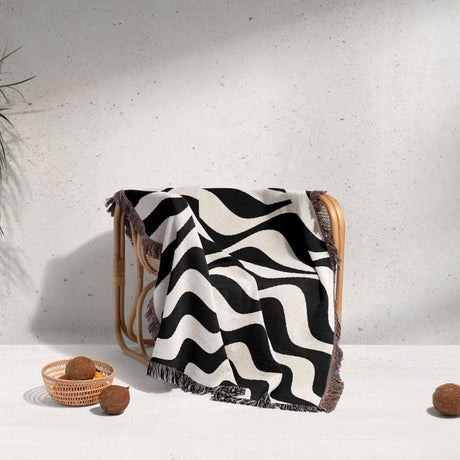 Black and white abstract wavey lines woven blanket throw tapestry draped over a wooden chair on a light gray background.