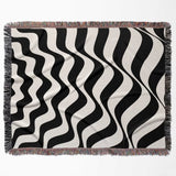 Black and white abstract wavey lines woven blanket throw tapestry flat lay on a plain background.