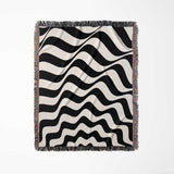 Black and white abstract wavey lines woven blanket throw tapestry with fringes full view on a light gray background.