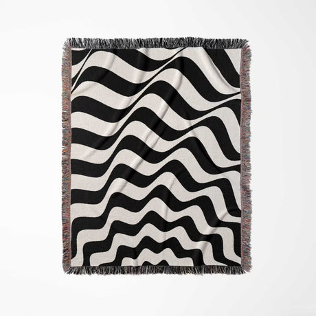 Black and white abstract wavey lines woven blanket throw tapestry with fringes full view on a light gray background.