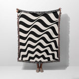 Black and white abstract wavey lines woven blanket throw tapestry held by a person on a white background.