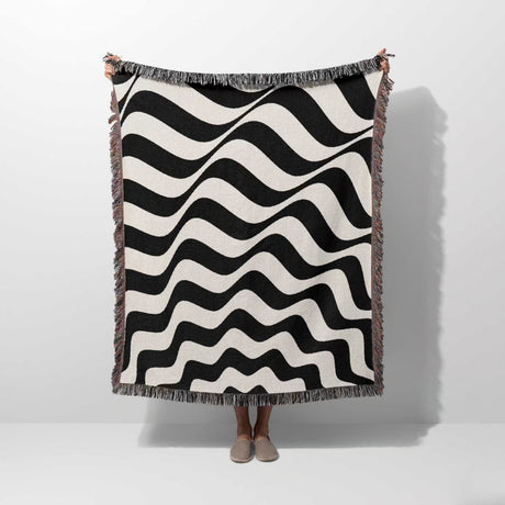 Black and white abstract wavey lines woven blanket throw tapestry held by a person on a white background.