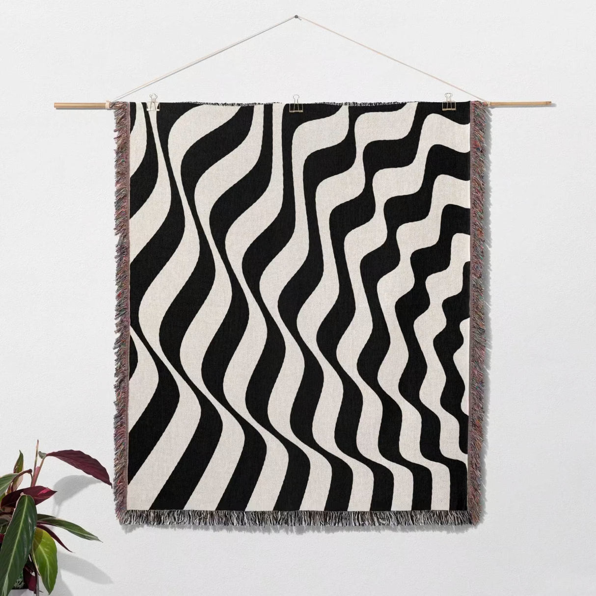 Black and white accent abstract waves woven blanket throw tapestry hanging on a wooden rod against a white wall.