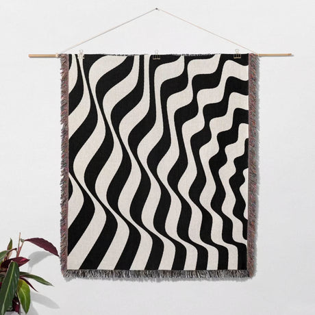 Black and white accent abstract waves woven blanket throw tapestry hanging on a wooden rod against a white wall.