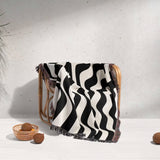 Black and white accent abstract waves woven blanket throw tapestry on a wooden chair against a light gray wall.